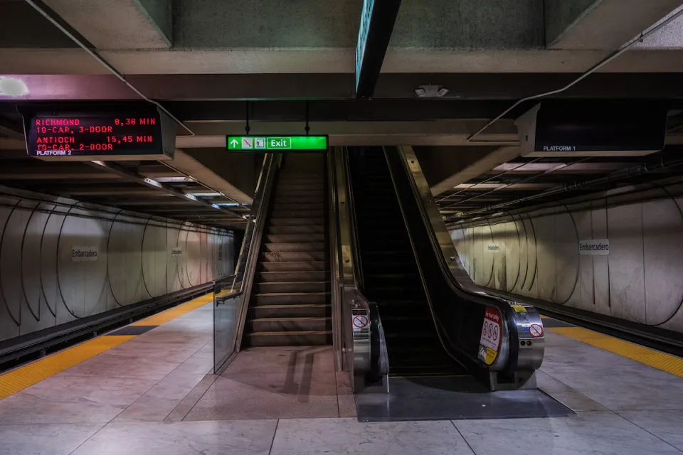 Empty underground Muni train platform in San Francisco with escalator, stairs in center of image.